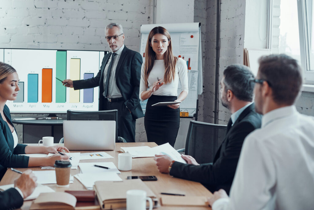 Executivos em reunião analisam gráfico de desempenho em tela durante apresentação de dados de treinamento corporativo