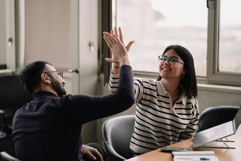 Dois colegas de trabalho comemorando com high five em um escritório
