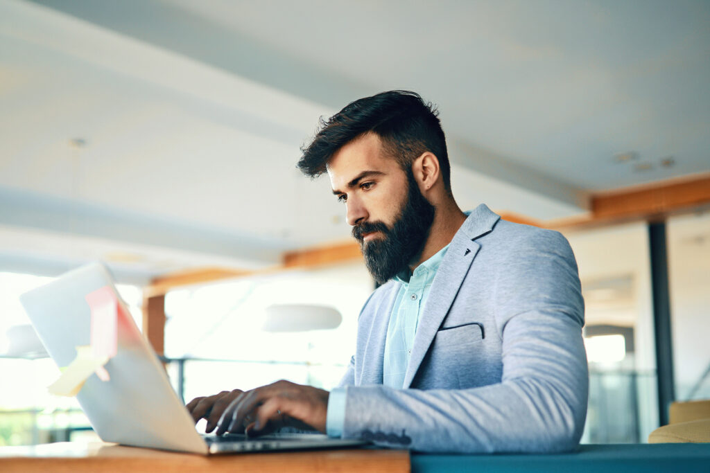 Gestor concentrado trabalhando no notebook em escritório moderno com luz natural, representando o dia a dia da liderança