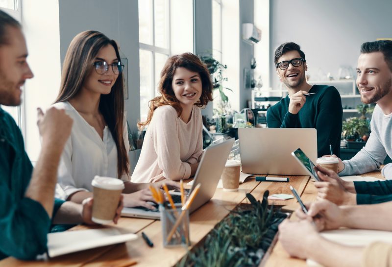 Equipe sorrindo durante reunião de trabalho com laptops e anotações sobre a mesa"